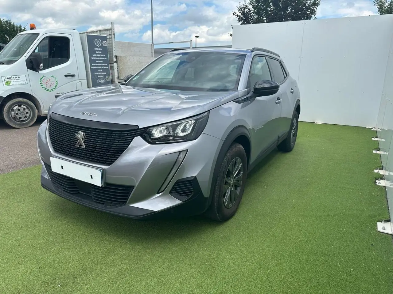 Peugeot 2008 gris clair en 3/4 avant droit, avec calandre noire et feux LED distinctifs.