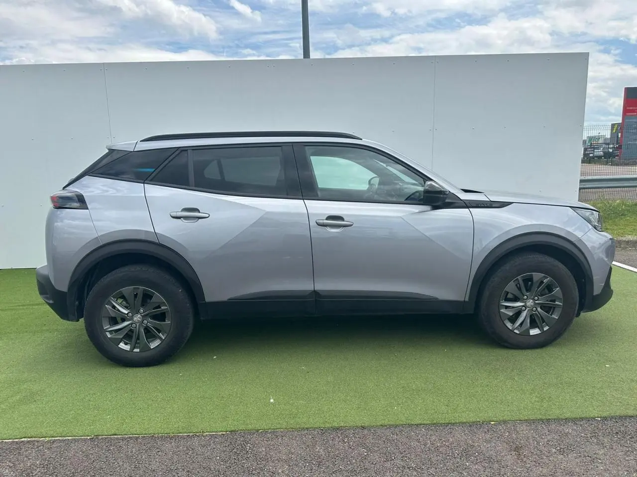 Peugeot 2008 gris clair vue de profil côté gauche, avec jantes alliage et barres de toit noires.