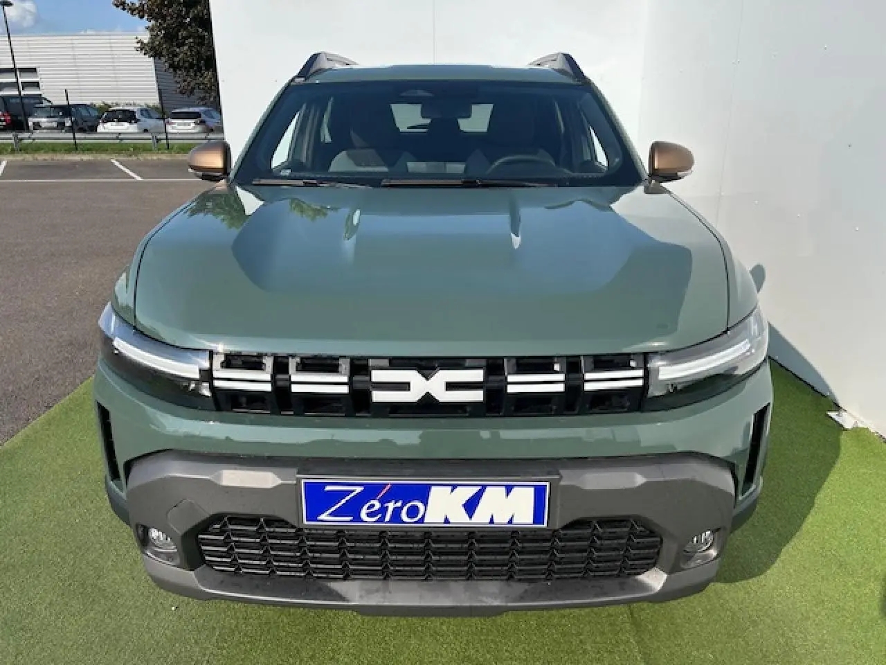 Vue frontale du Dacia Duster III hybride en kaki dusty avec calandre noire et logo central lumineux.