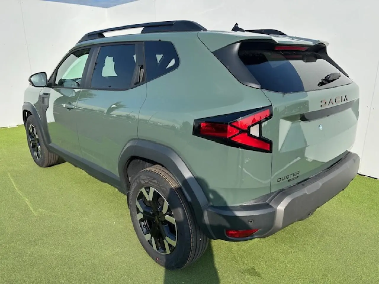 Vue 3/4 arrière droite du Dacia Duster III hybride en kaki dusty avec barres de toit noires et jantes alliage 17 pouces.
