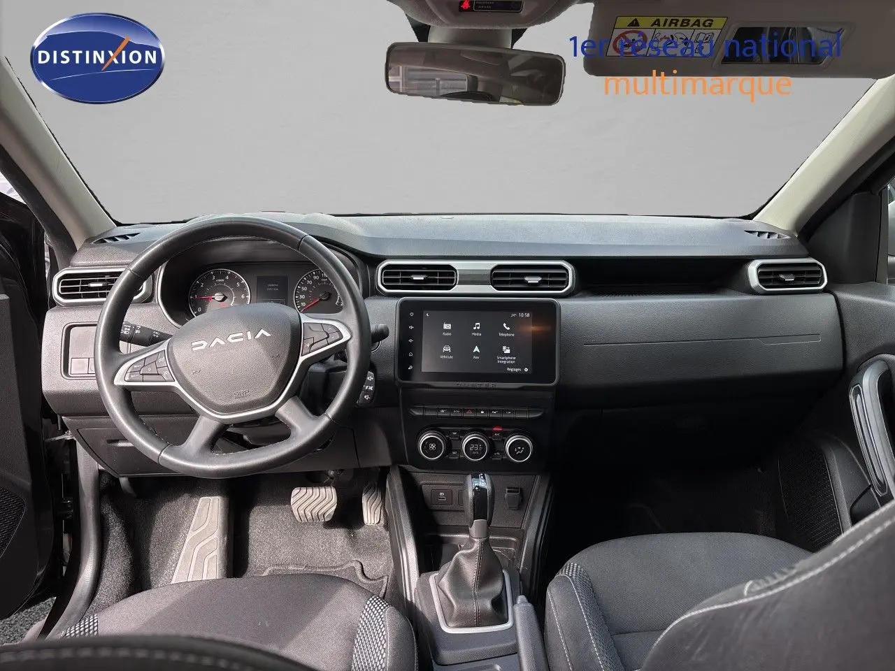 Vue intérieure côté conducteur du Dacia Duster 2024 noir, montrant le tableau de bord et les sièges en tissu noir.
