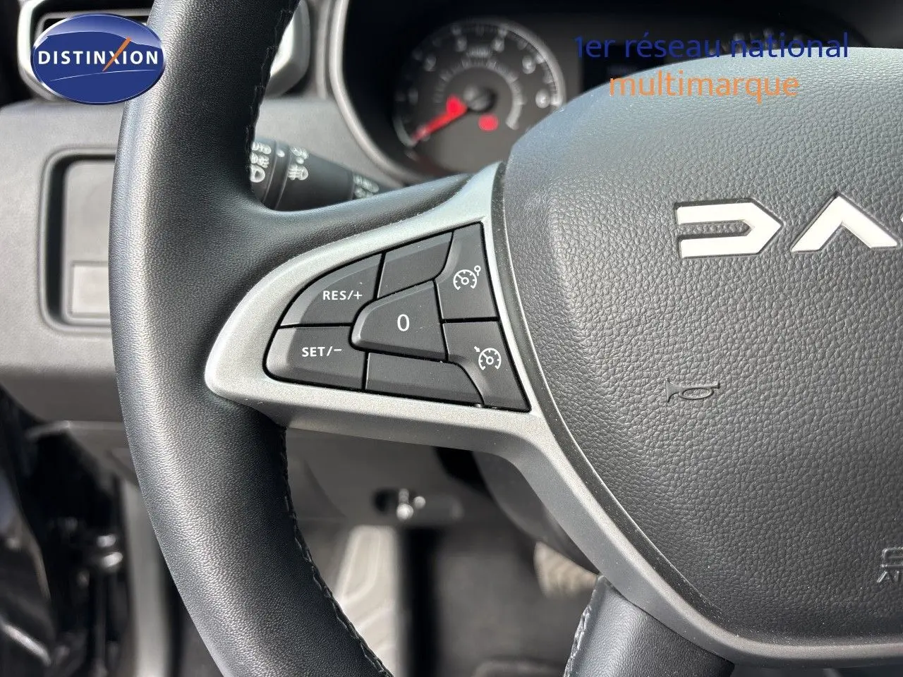 Gros plan sur le volant noir du Dacia Duster 2024 avec commandes intégrées côté gauche et logo partiel visible.