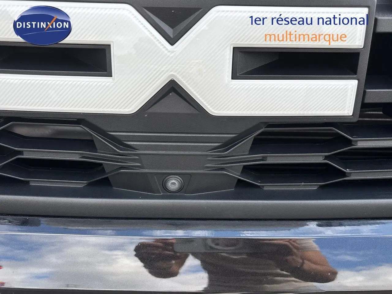 Gros plan sur la calandre noire du Dacia Duster 2024 avec caméra frontale intégrée sous le logo.