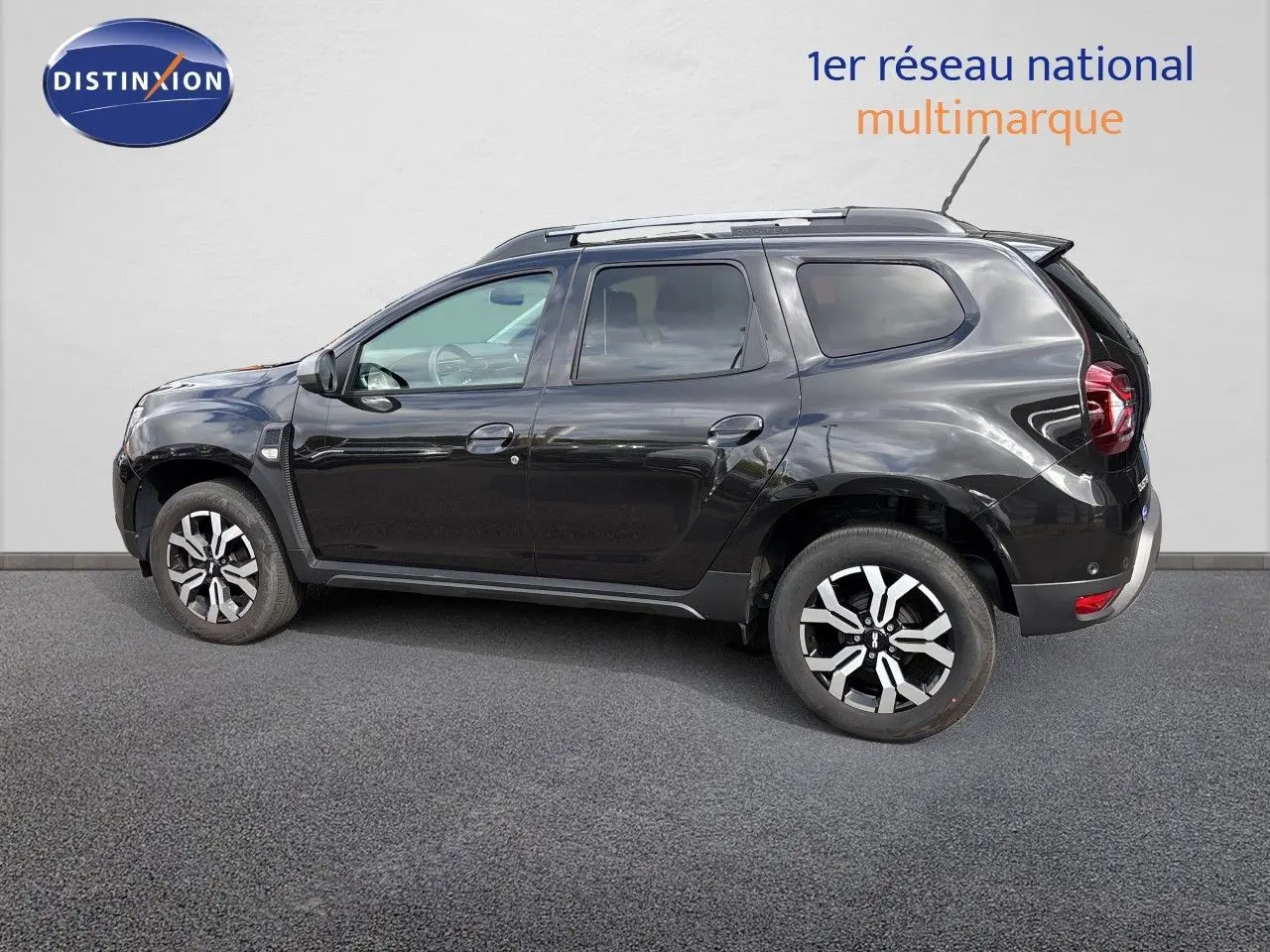 Profil droit du Dacia Duster noir 2024 avec jantes bi-ton et toit équipé de barres de toit.
