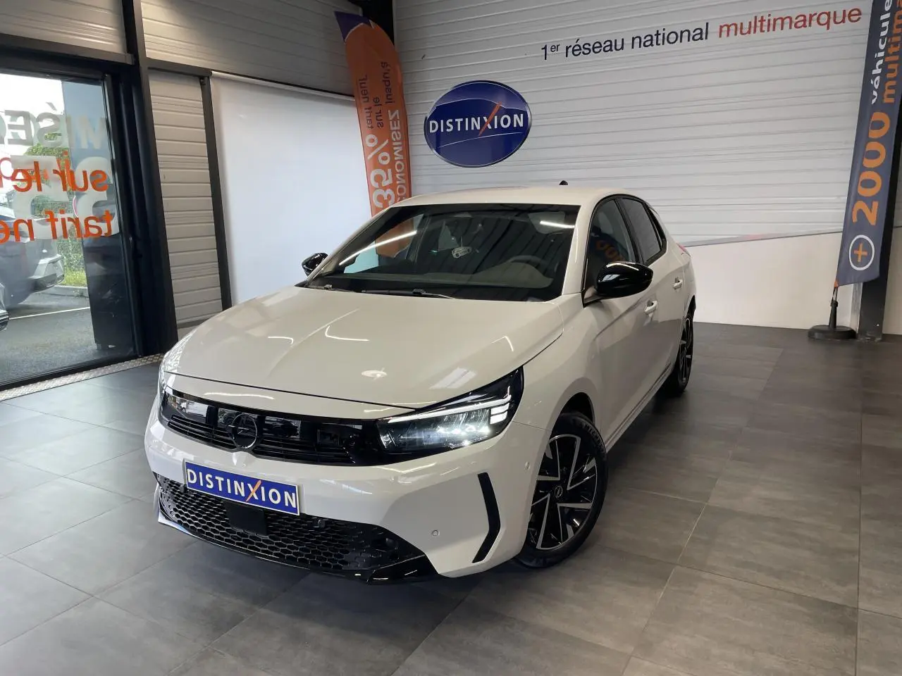 Opel Corsa blanche vue 3/4 avant droit en showroom, avec calandre noire et jantes alliage noires diamantées.