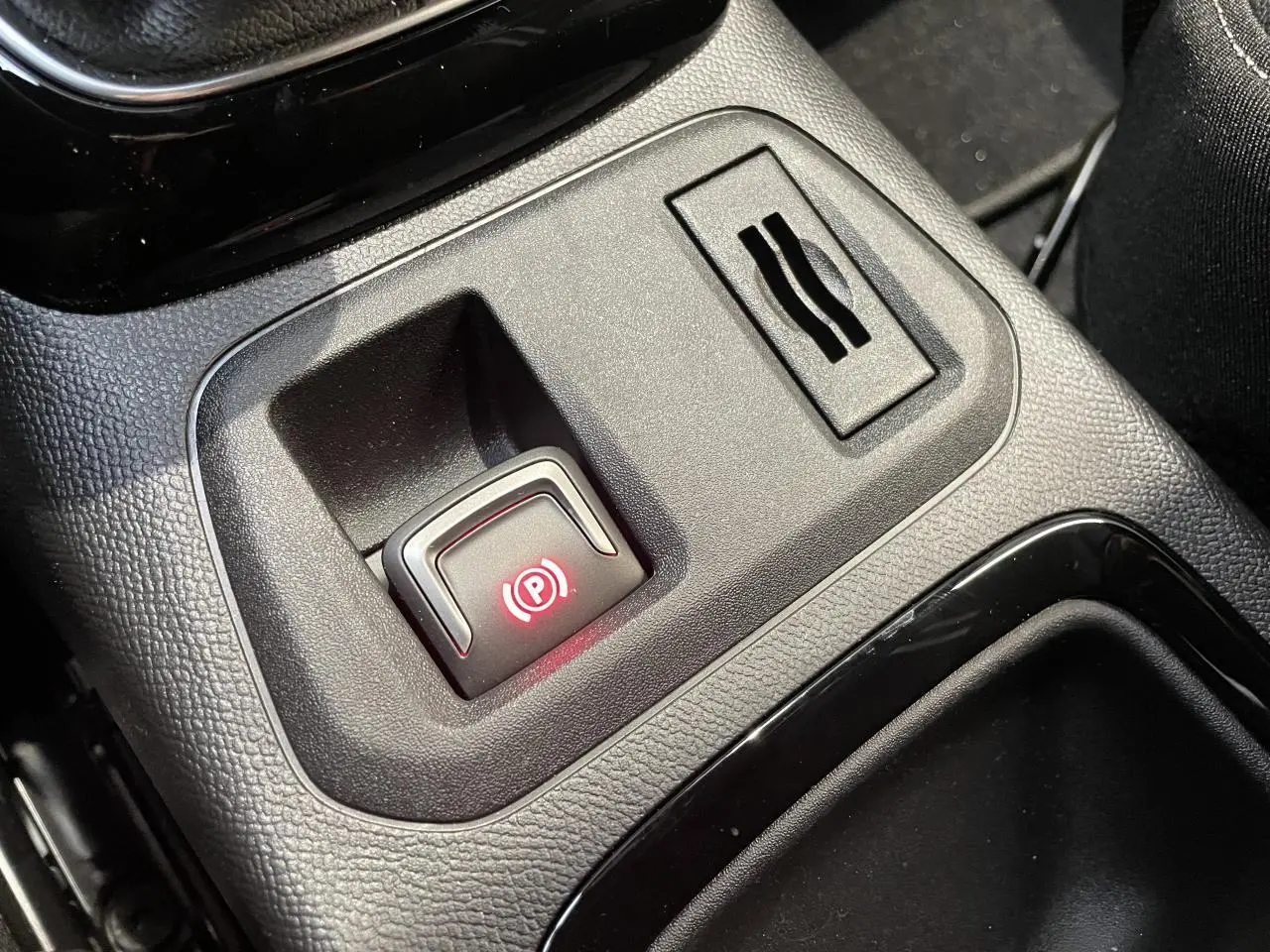 Gros plan sur le frein de parking électrique illuminé en rouge dans la console centrale noire de l'Opel Corsa blanche.
