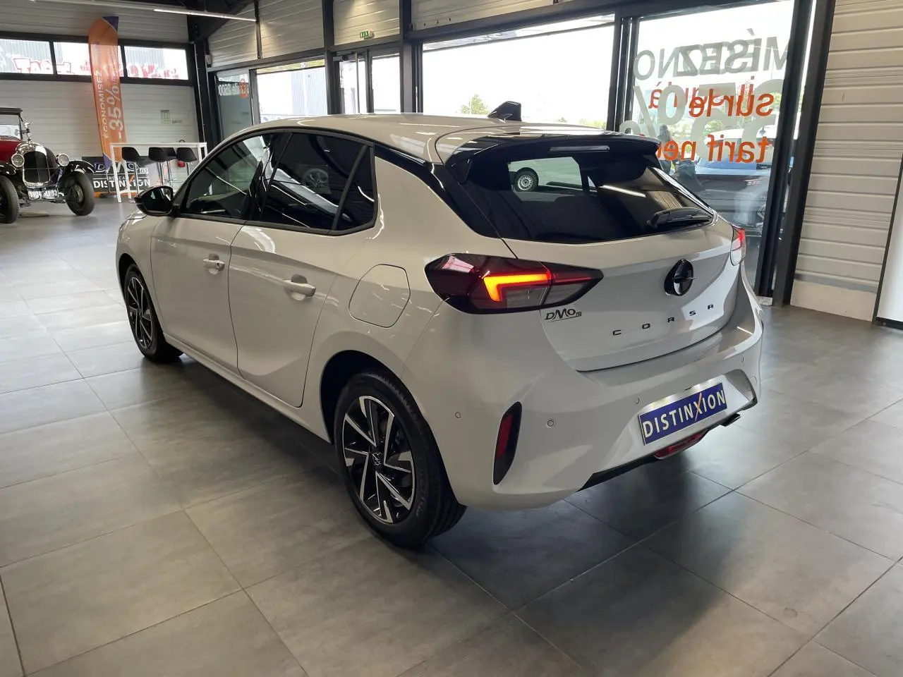 Opel Corsa blanche vue 3/4 arrière droit en intérieur, avec feux arrière LED allumés et jantes alliage noires.