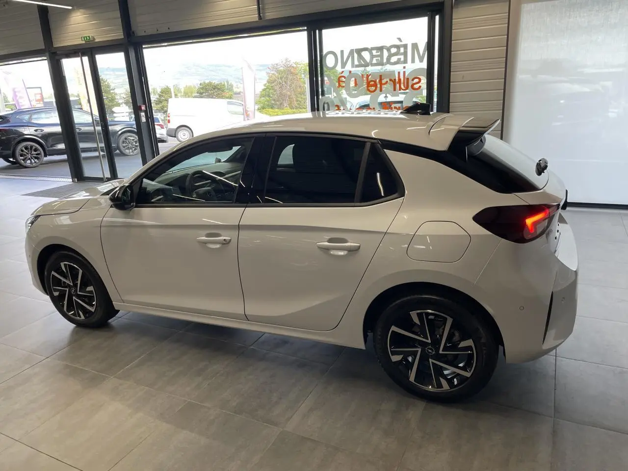Opel Corsa blanc vue de profil côté gauche en intérieur, vitres surteintées et jantes alliage noires.