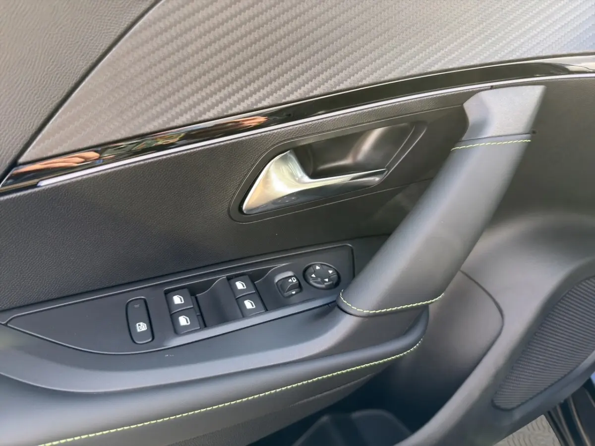 Gros plan sur la porte intérieure côté conducteur du Peugeot 2008 Hybrid 145 e-DCS6 GT, avec surpiqûres vertes et commandes électriques.