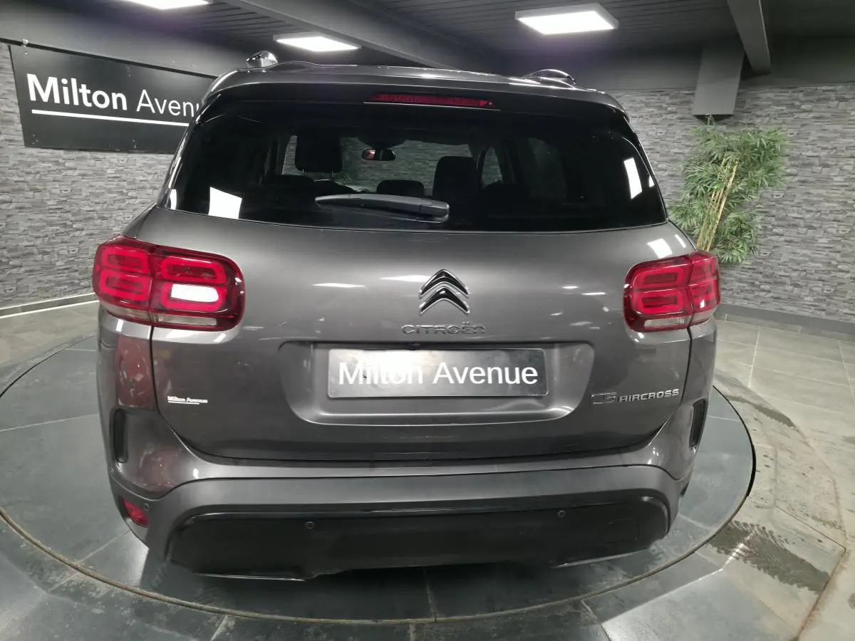 Vue arrière d'un Citroën C5 Aircross gris métallisé avec feux arrière LED et hayon fermé en showroom.