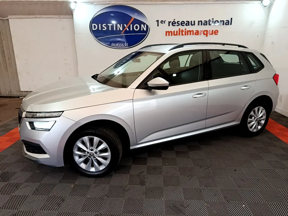 SKODA KAMIQ gris clair vu de profil côté gauche, intérieur showroom avec logo Distinxion en arrière-plan.