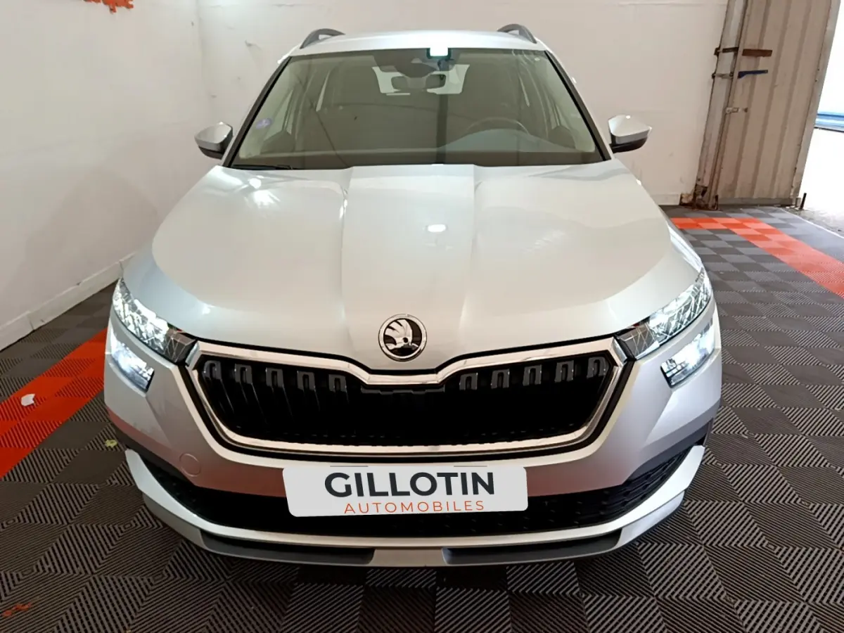 Vue frontale d'un Skoda Kamiq gris clair 2022 avec calandre noire et phares LED allumés dans un garage.