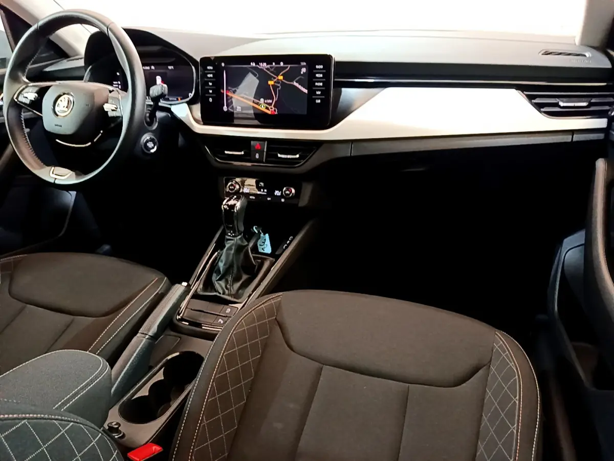 Intérieur du Skoda Kamiq 2022 vu de l'avant, sièges noirs avec surpiqûres, tableau de bord moderne et écran tactile central.