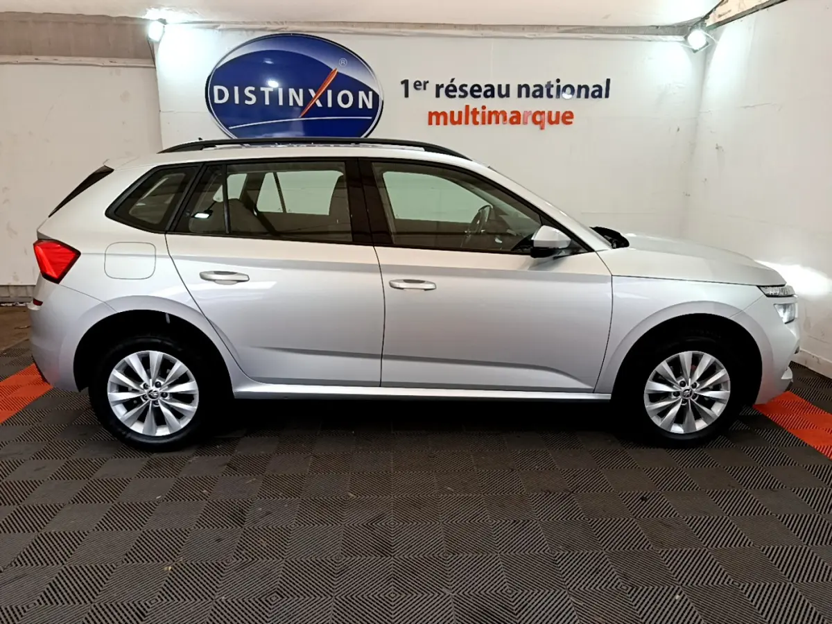 Vue latérale droite d'un Skoda Kamiq gris clair 2022 garé en intérieur avec rails de toit noirs visibles.