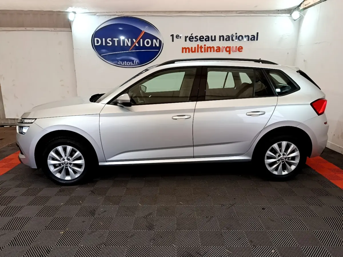 Vue de profil côté gauche d'un Skoda Kamiq gris clair 2022 avec jantes alliage et barres de toit noires.