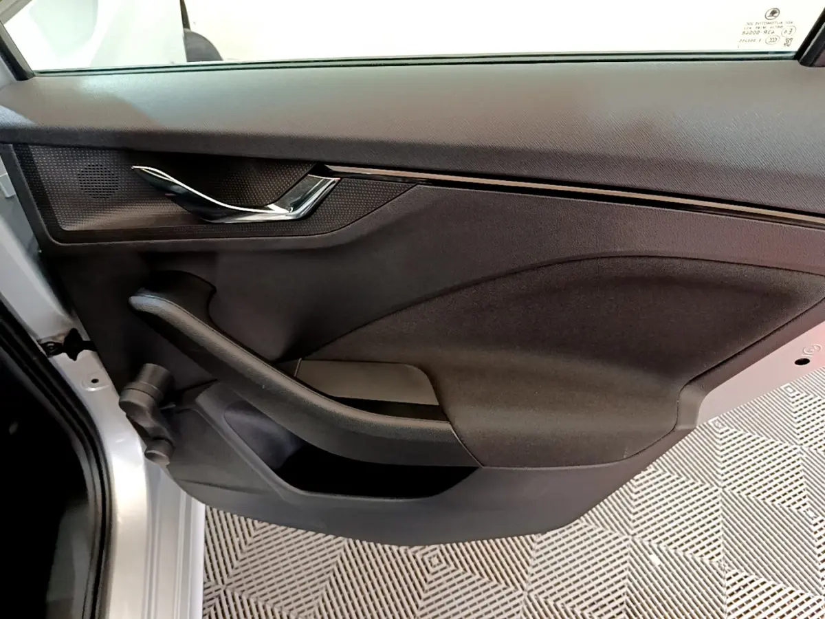 Gros plan sur la porte intérieure côté gauche du Skoda Kamiq gris clair, avec poignée chromée et panneau noir texturé.