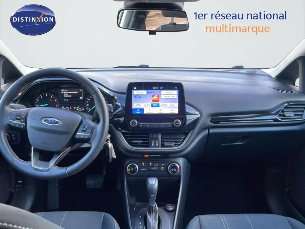 Vue intérieure avant centrée sur le tableau de bord et volant de la Ford Fiesta blanche avec écran tactile et boîte auto.