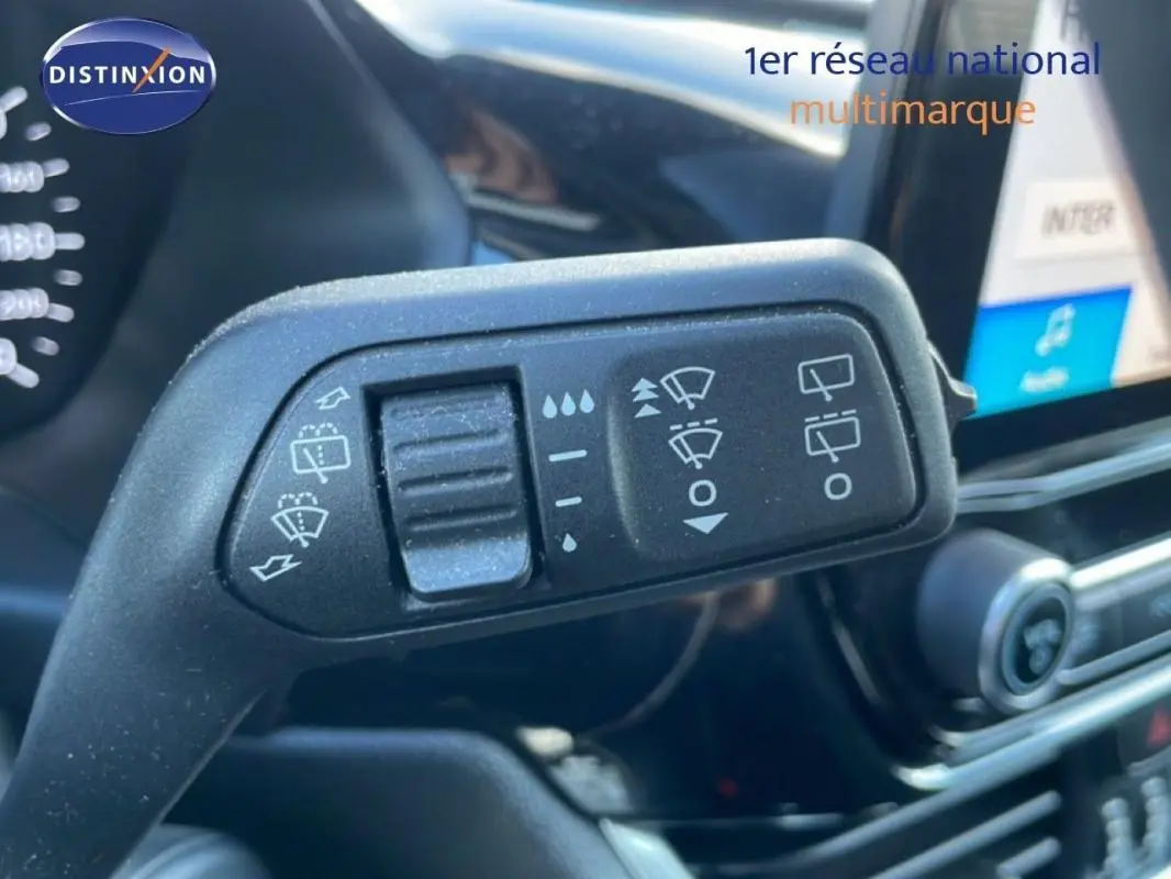 Gros plan sur la commande d’essuie-glace dans l’habitacle d’une Ford Fiesta blanche, avec écran tactile en arrière-plan.