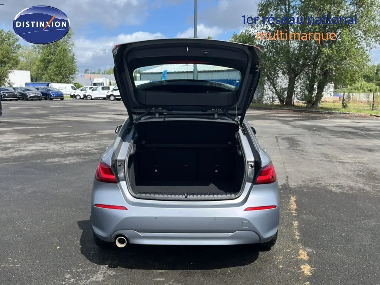 Vue arrière d'une BMW Série 1 116i 2022 en gris mat avec coffre ouvert sur un parking extérieur.