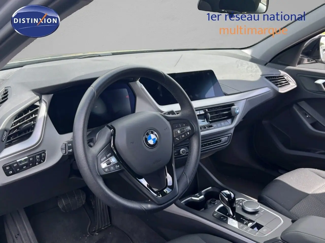 Vue intérieure côté conducteur de la BMW Série 1 116i 2022, volant cuir et tableau de bord moderne gris noir.