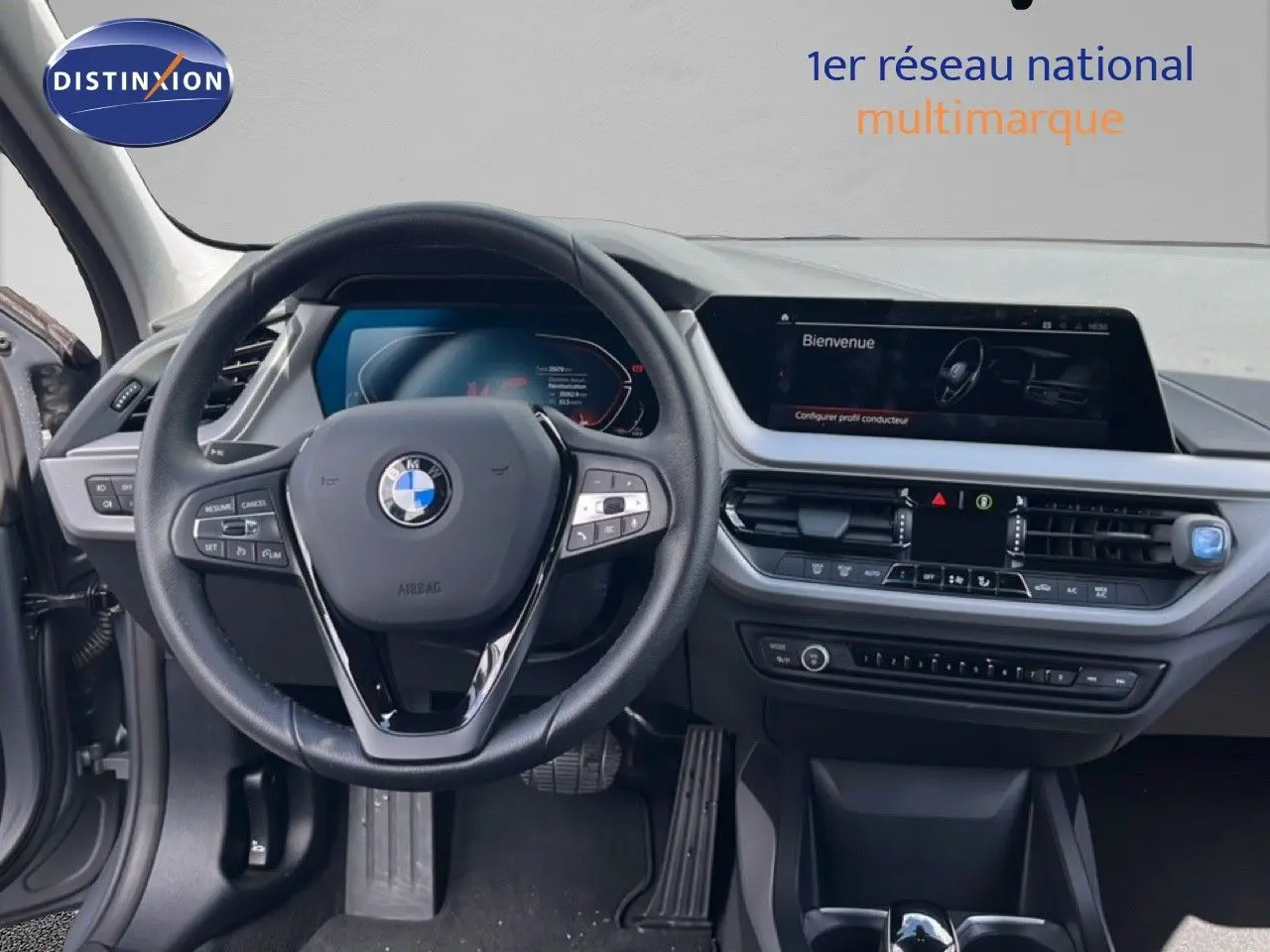 Vue intérieure centrée sur le volant BMW et le tableau de bord moderne avec écran tactile, ambiance gris noir.