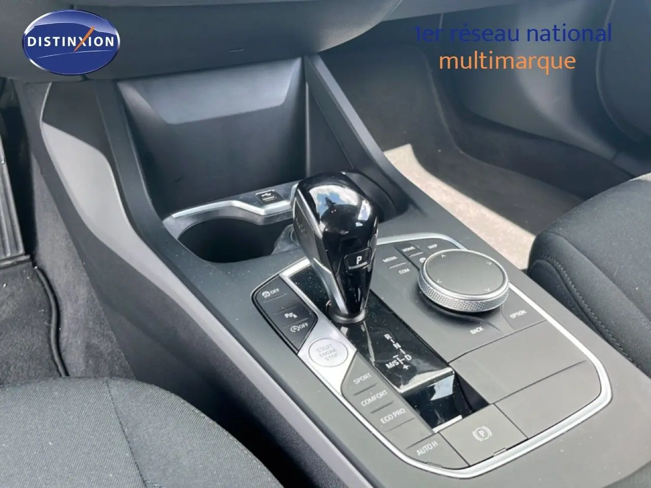 Gros plan sur la console centrale avec levier de vitesse et commandes, intérieur tissu gris de la BMW Série 1 116i 2022.