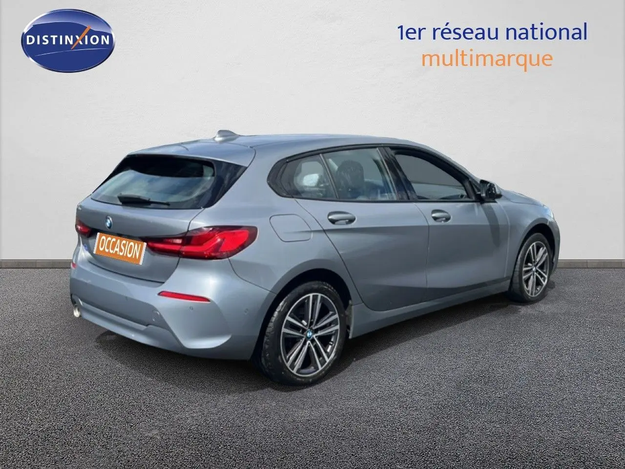 Vue 3/4 arrière droite d'une BMW Série 1 116i 2022 en gris mat Frozen Pure Grey avec jantes alliage bicolores.