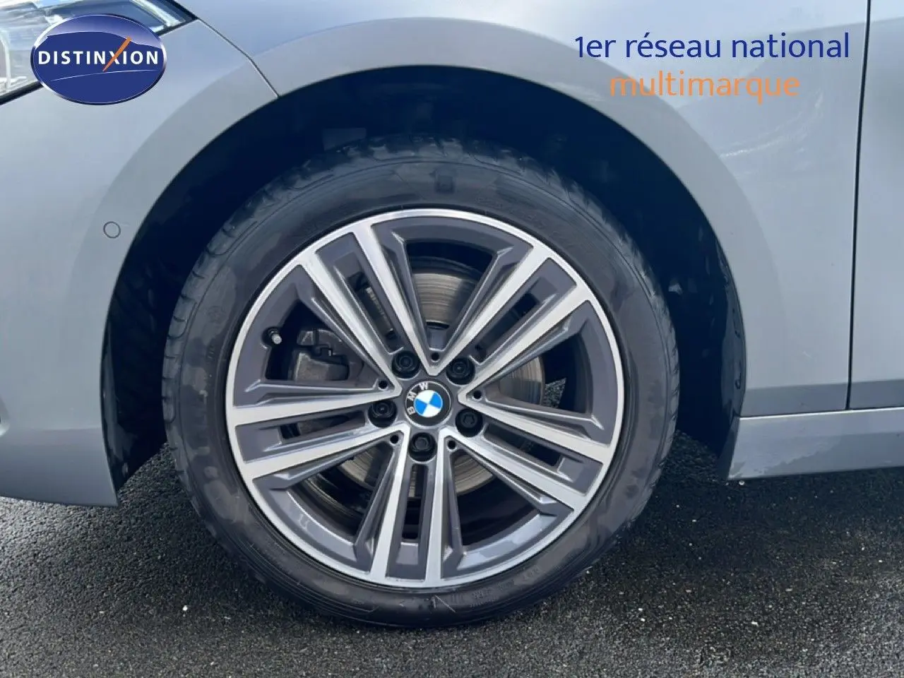 Gros plan sur la roue avant gauche d’une BMW Série 1 116i 2022 en gris Frozen Pure avec jante alliage bicolore.