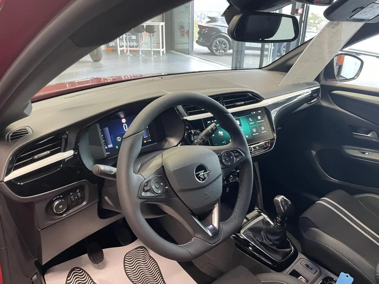 Vue intérieure côté conducteur de l’Opel Corsa rouge 2026, volant cuir, écran tactile 10 pouces et boîte manuelle.