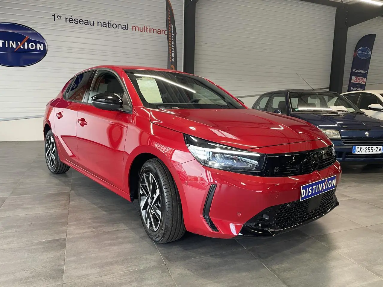 Opel Corsa rouge vue 3/4 avant droit en intérieur avec calandre noire et jantes alliage diamantées.
