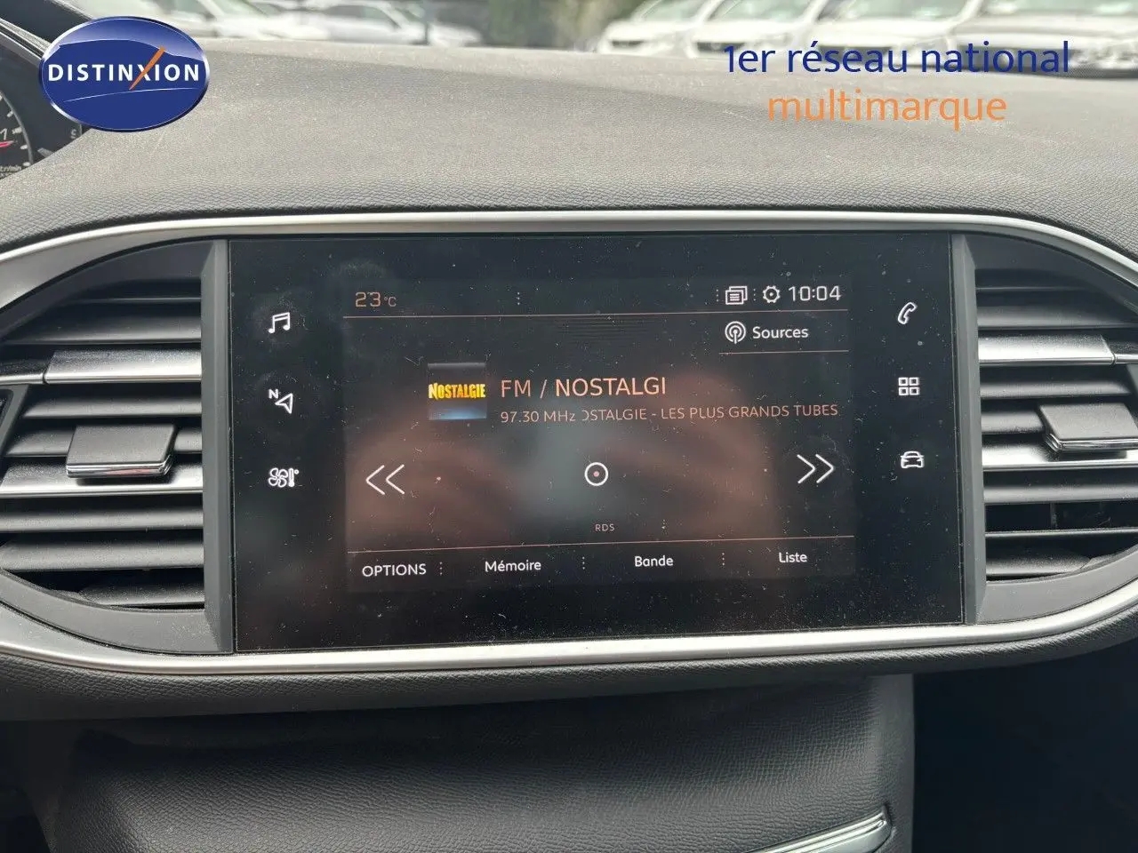 Écran tactile central du tableau de bord de la Peugeot 308 Bleu Magnetic affichant la radio FM Nostalgie à 10h04.