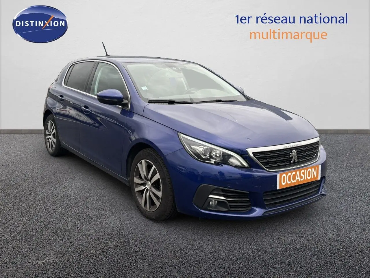 Peugeot 308 bleu Magnetic vue 3/4 avant droit avec calandre chromée et plaque "OCCASION" orange.