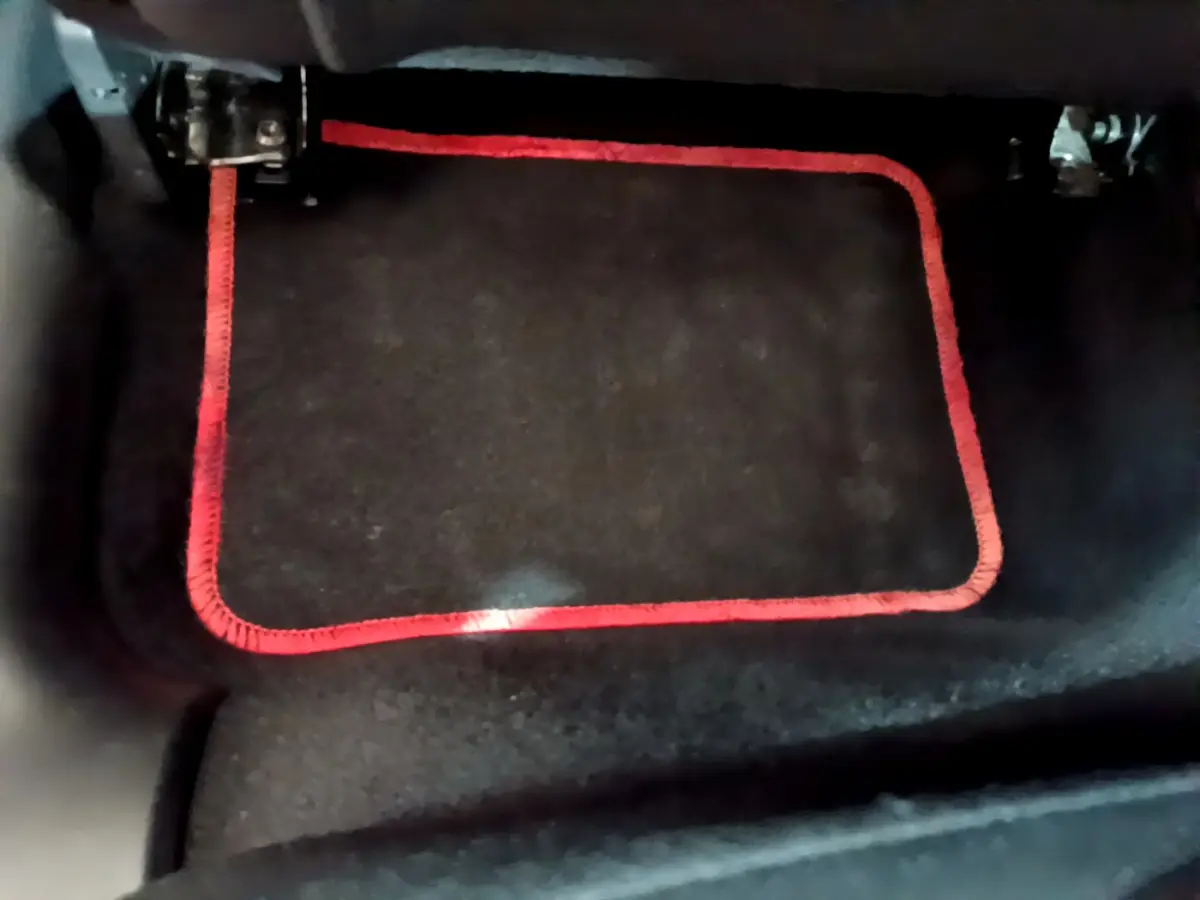 Gros plan sur le tapis de sol noir avec bordure rouge dans l'habitacle d'une Citroën C3 blanche.