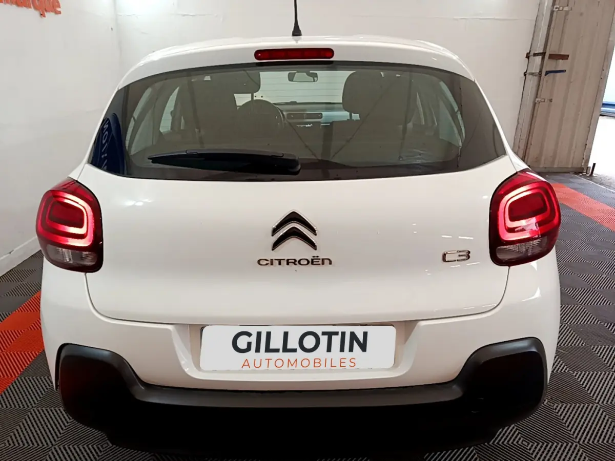 Vue arrière d'une Citroën C3 blanche de 2018 avec feux arrière allumés dans un garage fermé.