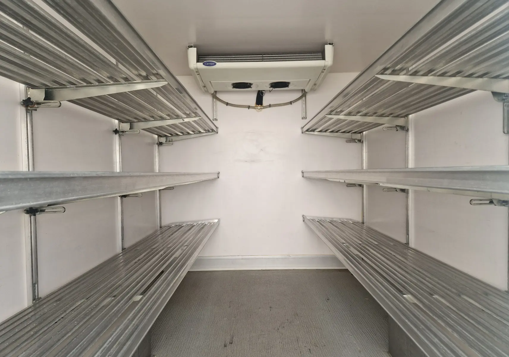 Intérieur isotherme blanc du Renault Master Plancher Cabine, vue frontale des étagères métalliques et groupe frigo Carrier au plafond.