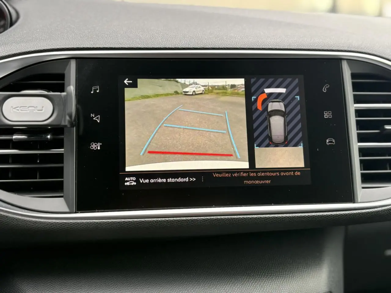 Écran tactile central affichant la caméra de recul et l'aide au stationnement de la Peugeot 308 blanche nacrée, vue intérieure.