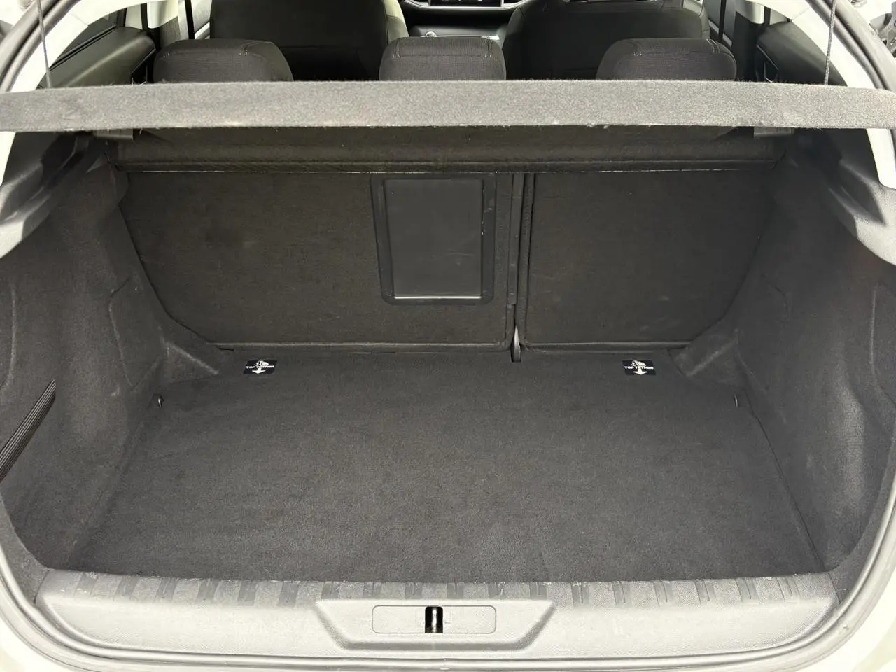 Vue du coffre ouvert d'une Peugeot 308 blanc nacré, montrant un espace de rangement propre et spacieux.