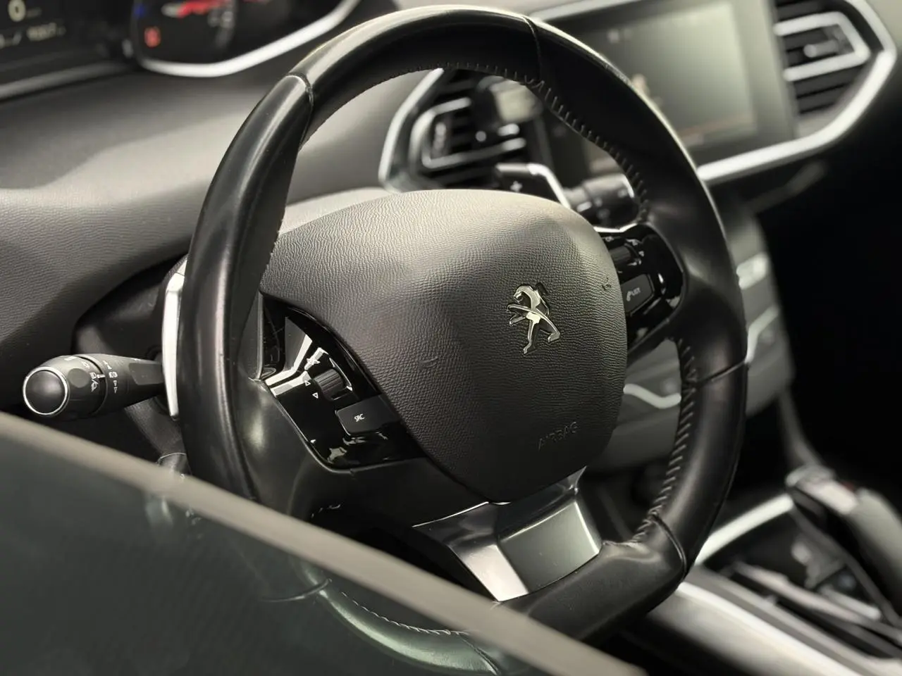 Gros plan sur le volant cuir noir multifonctions d'une Peugeot 308 1.2 PureTech 130 Allure, intérieur moderne.