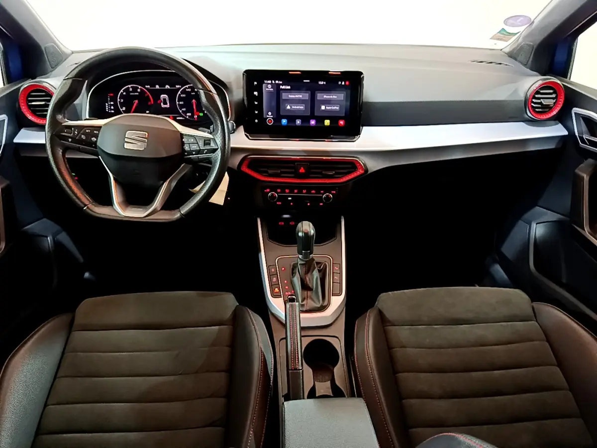 Vue intérieure avant du tableau de bord et volant de la SEAT Arona 2022, avec touches rouges et écran tactile central.