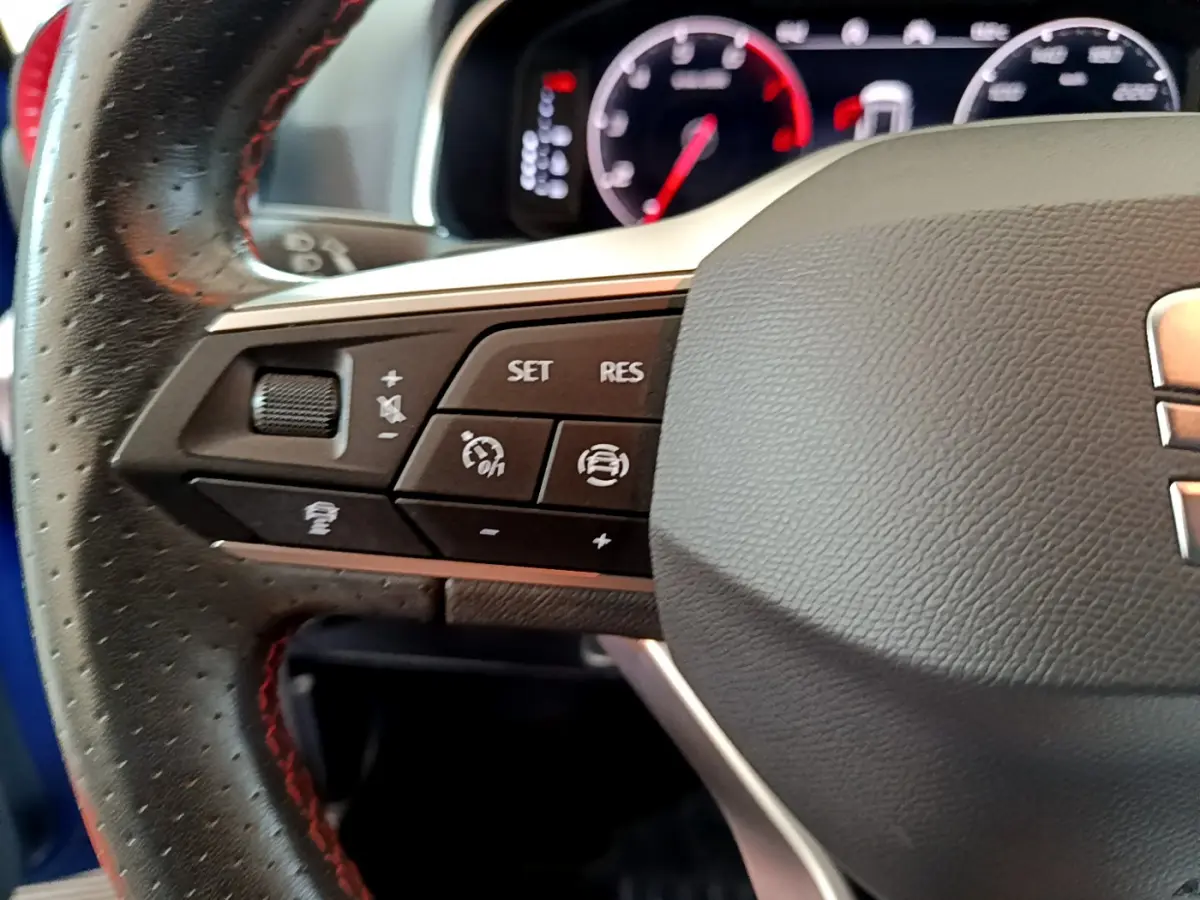 Gros plan sur le volant cuir noir avec commandes multifonctions du SEAT Arona bleu 2022, tableau de bord numérique visible.