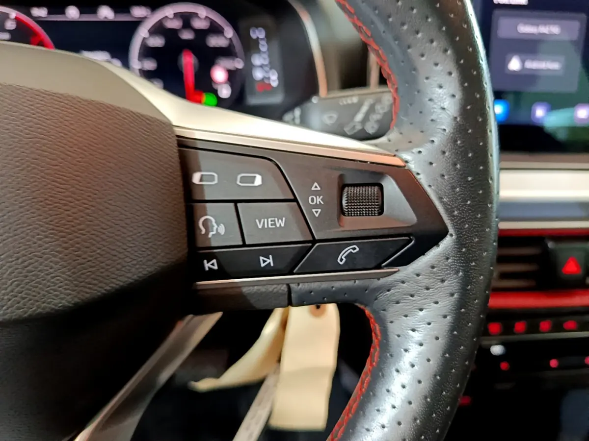 Gros plan sur les commandes du volant en cuir noir perforé avec surpiqûres rouges du SEAT Arona 2022.