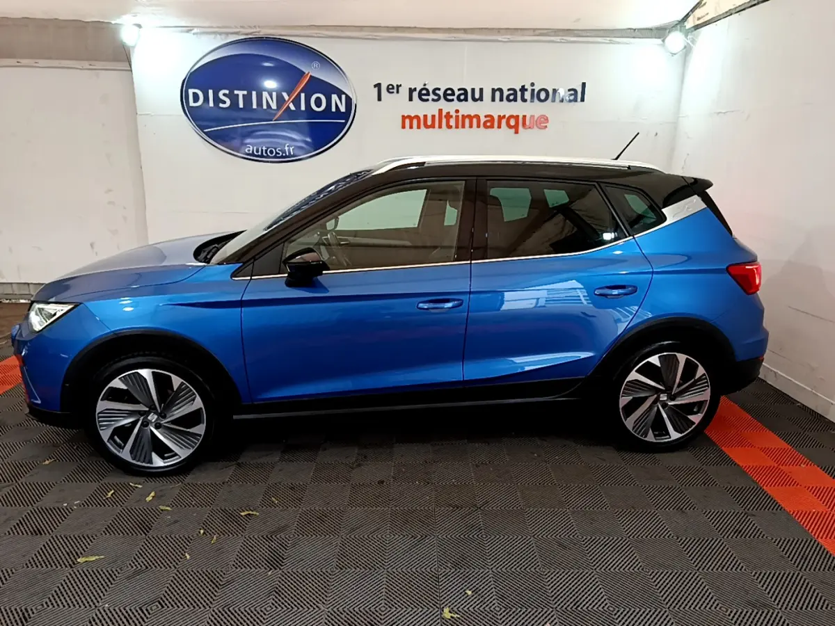 Profil côté gauche d'un SEAT Arona bleu 2022 avec toit noir et jantes alliage distinctives en intérieur showroom.