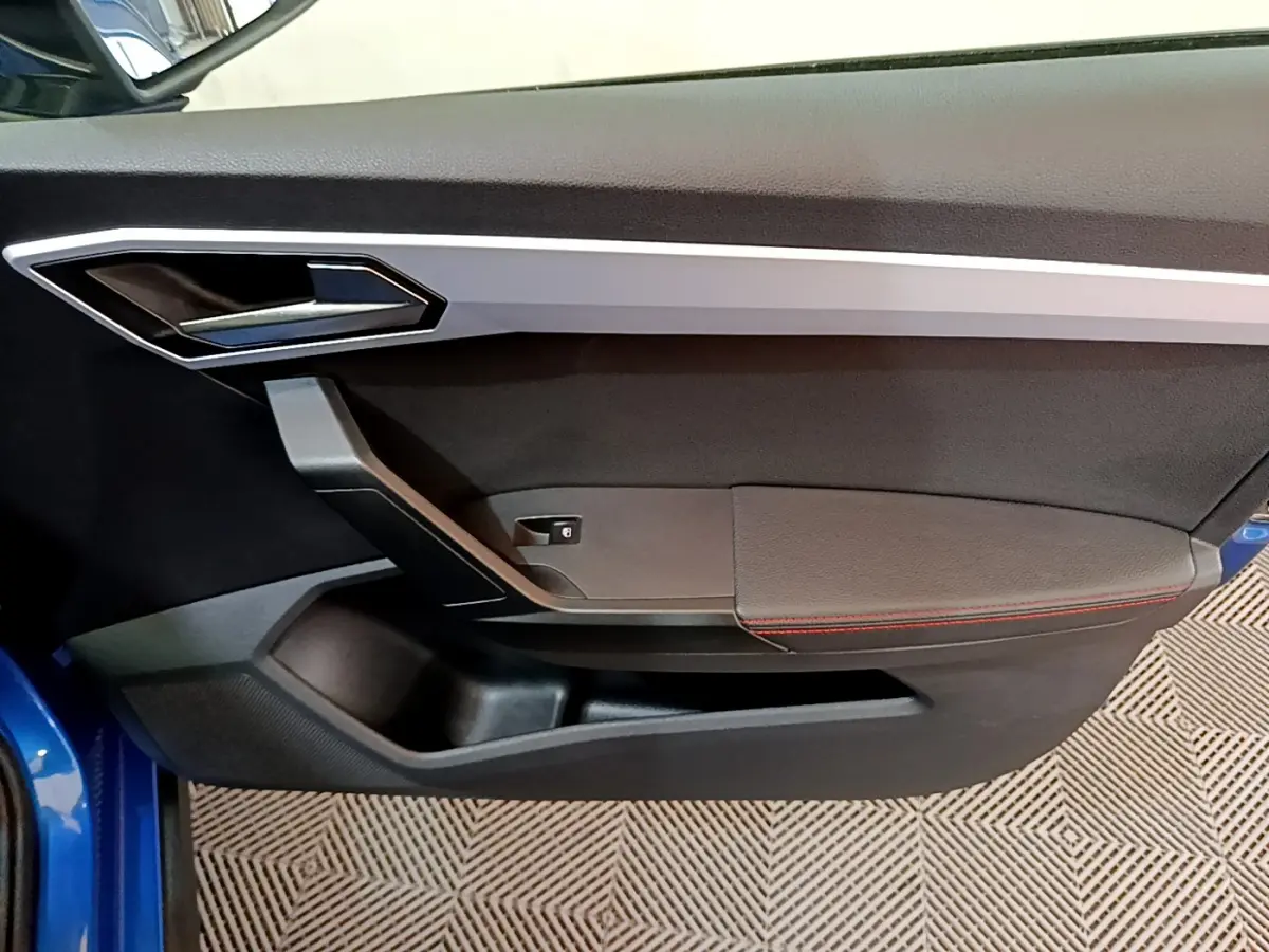 Gros plan sur la porte côté gauche du SEAT Arona bleu 2022, avec poignée argentée et surpiqûres rouges.