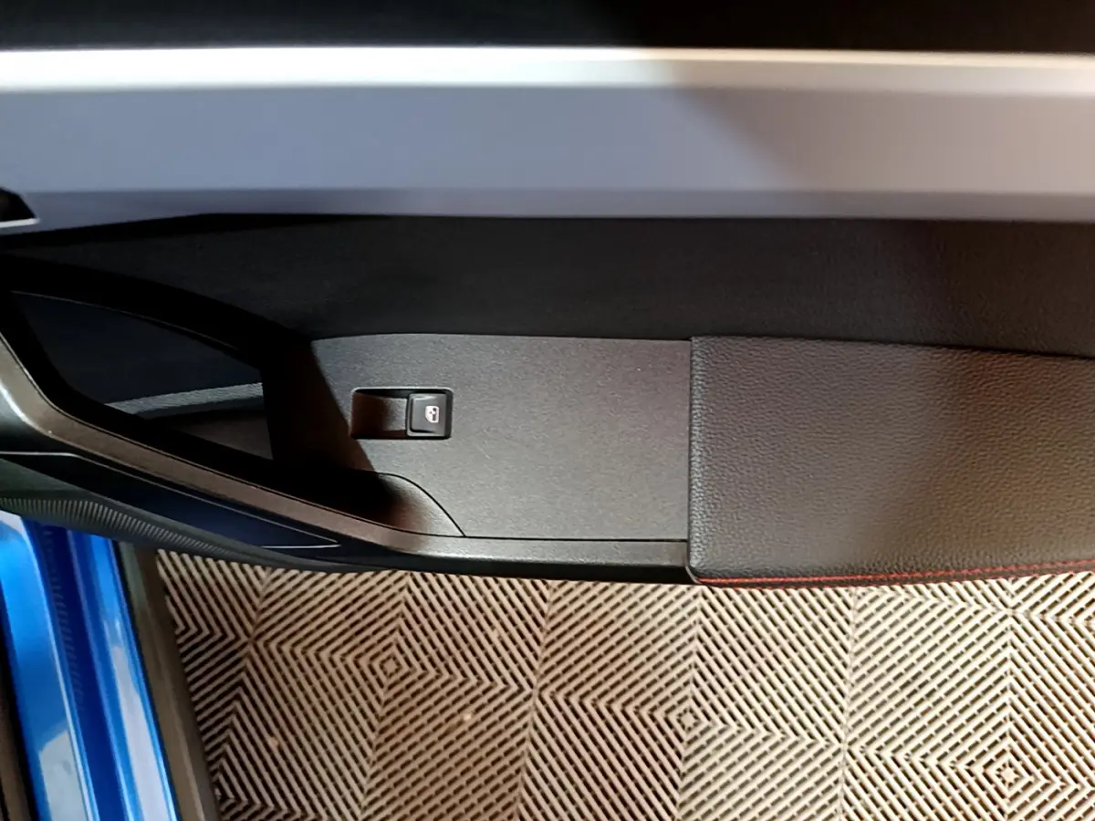 Détail de la porte côté gauche du SEAT Arona bleu 2022 avec bouton de verrouillage intégré et surpiqûres rouges.