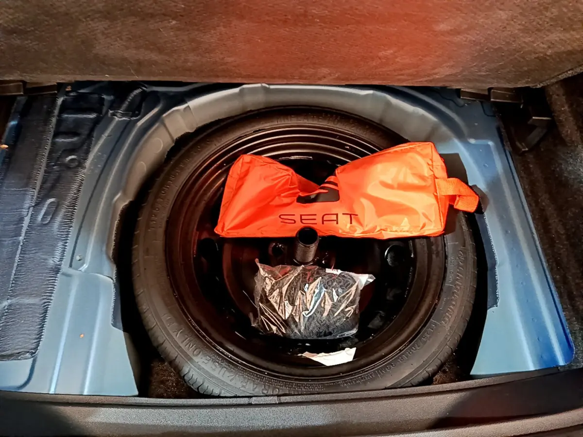 Vue plongeante sur la roue de secours noire dans le coffre bleu du SEAT Arona avec sac orange marqué SEAT.