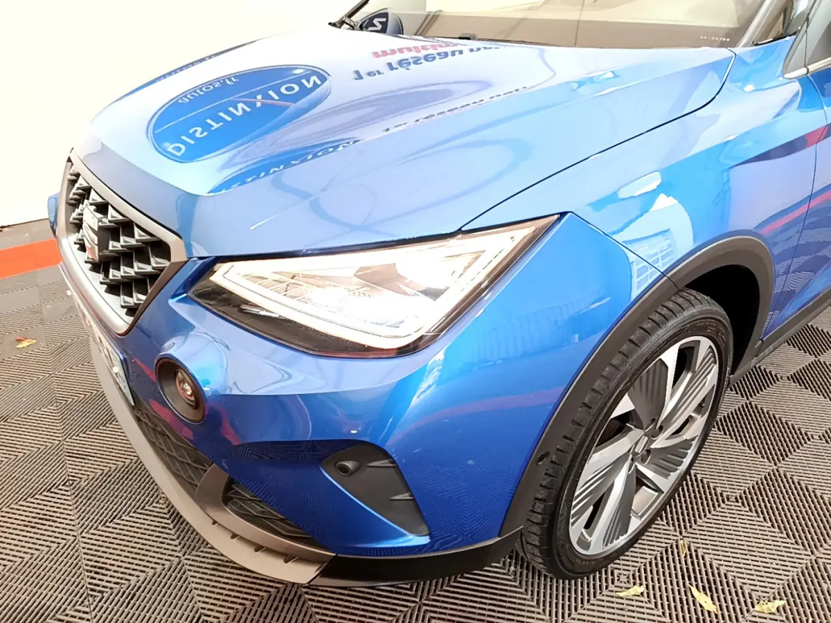 Vue rapprochée 3/4 avant droit du SEAT ARONA bleu 2022, mettant en valeur le phare LED et la calandre distinctive.
