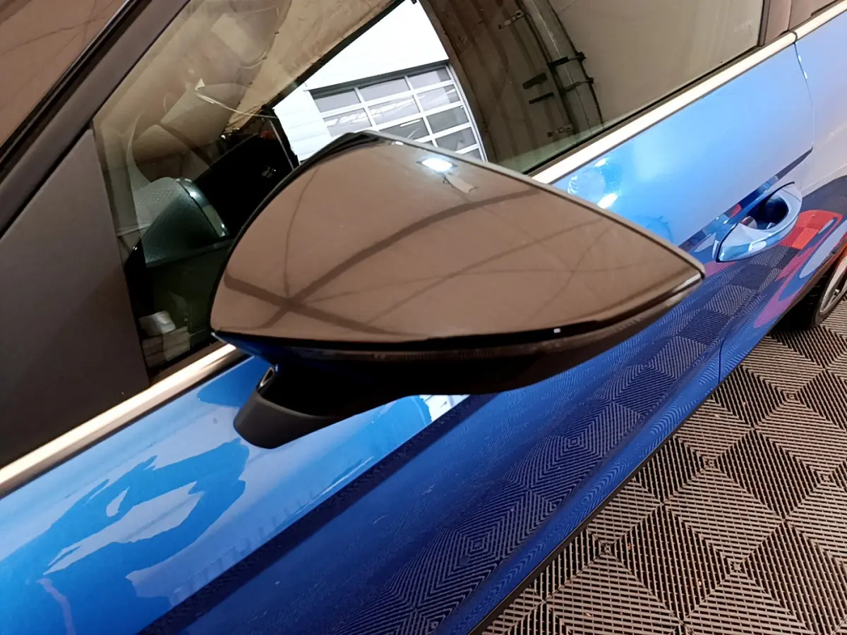 Rétroviseur côté gauche en gros plan sur SEAT Arona bleu, avec poignée de porte et reflet intérieur visibles.