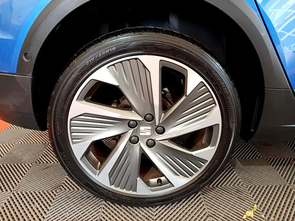 Gros plan sur la roue avant droite d'une SEAT Arona bleue, mettant en valeur la jante aluminium au design moderne.