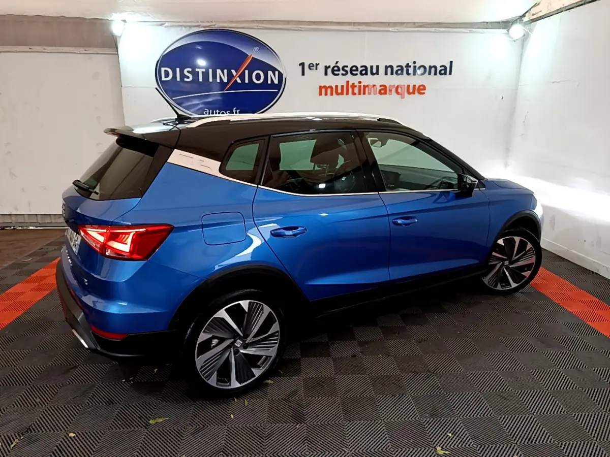 SEAT Arona bleu en vue 3/4 arrière droit, toit noir contrasté et jantes alliage distinctives dans un showroom