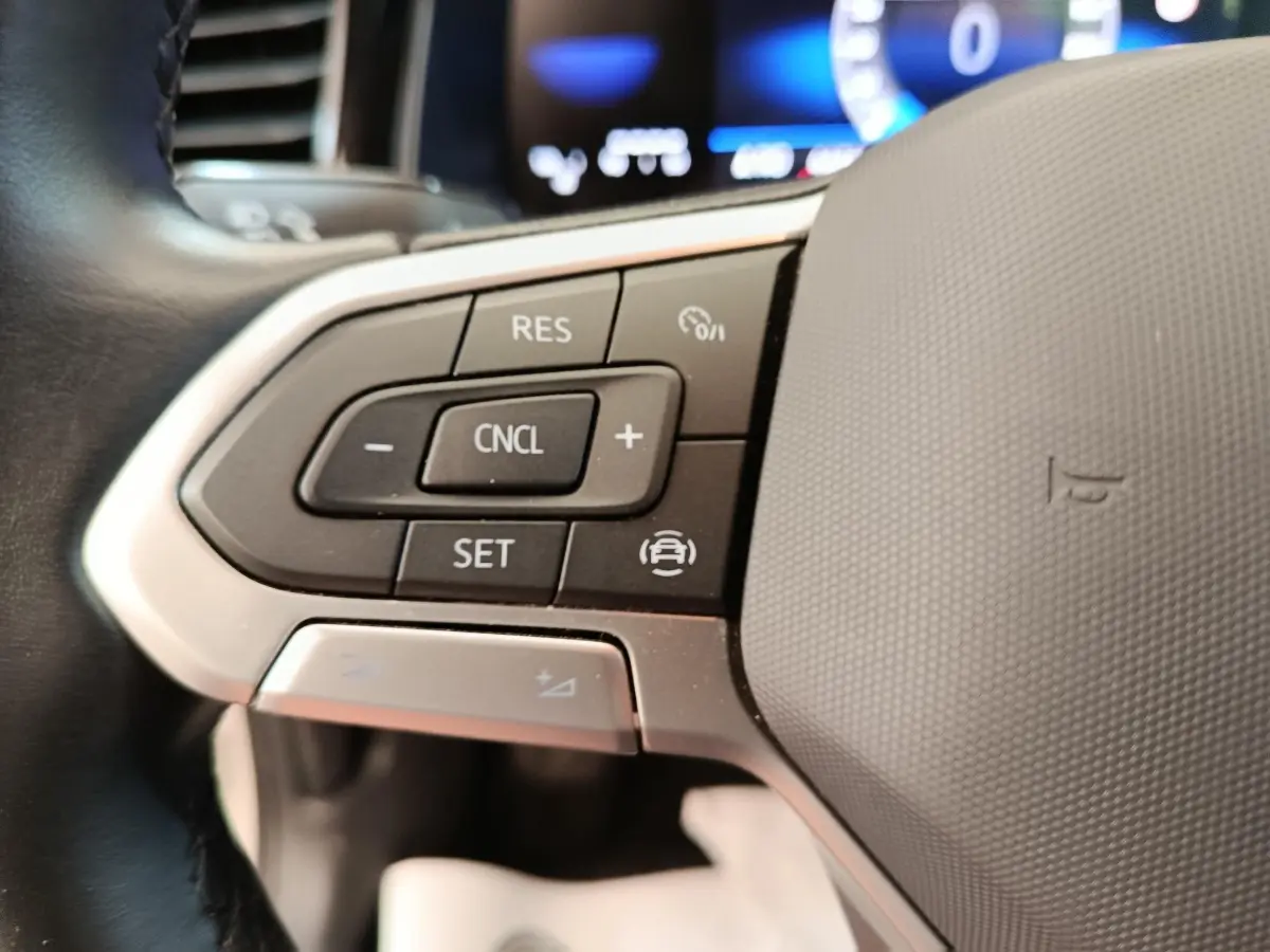 Gros plan sur le volant multifonctions en cuir et alu de la Volkswagen Polo gris clair 2023, avec commandes de régulateur.